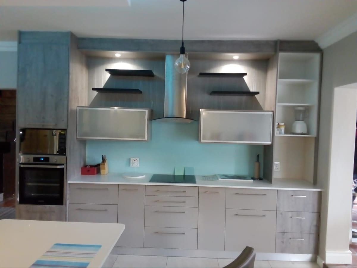 Grey wood-grain wall of cabinetry with frosted-glass wall units, open shelving, a chimney extractor and a built-in oven.